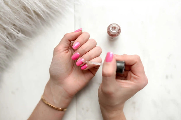 Pink manicured nails being painted.